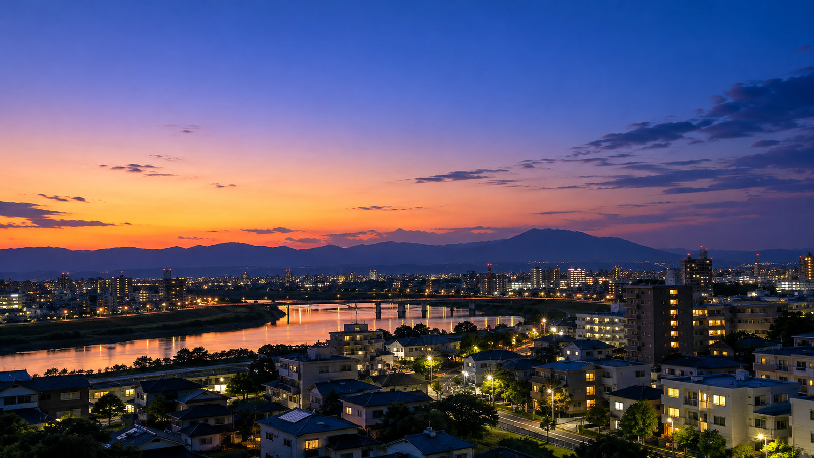 日の入り後も明るさが残る空と、街の灯りがともり始めた夕暮れの風景（イメージ画像）